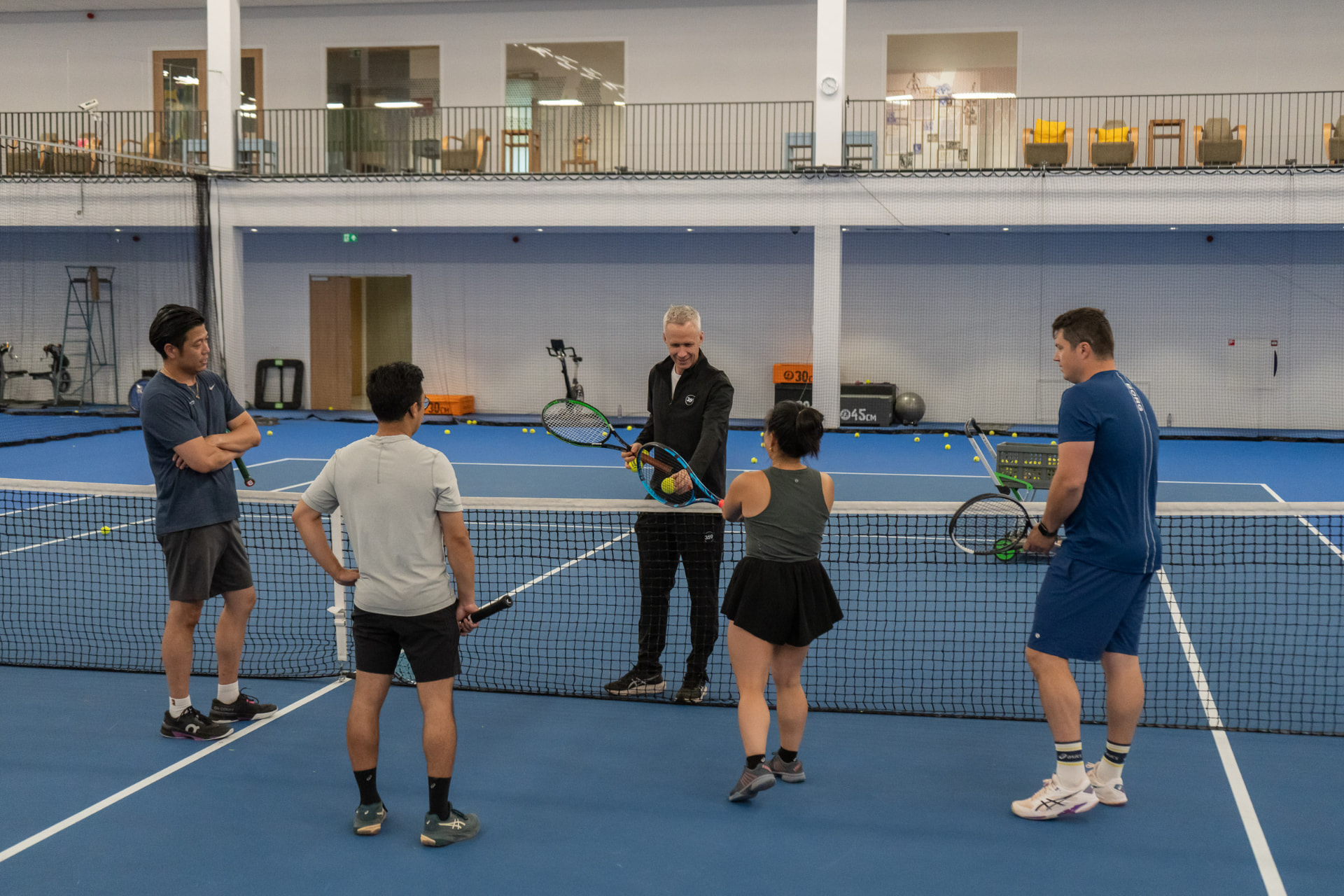 Coach geeft uitleg aan groep volwassenen bij het net op indoorbaan NTC Amstelveen — 359.tennis