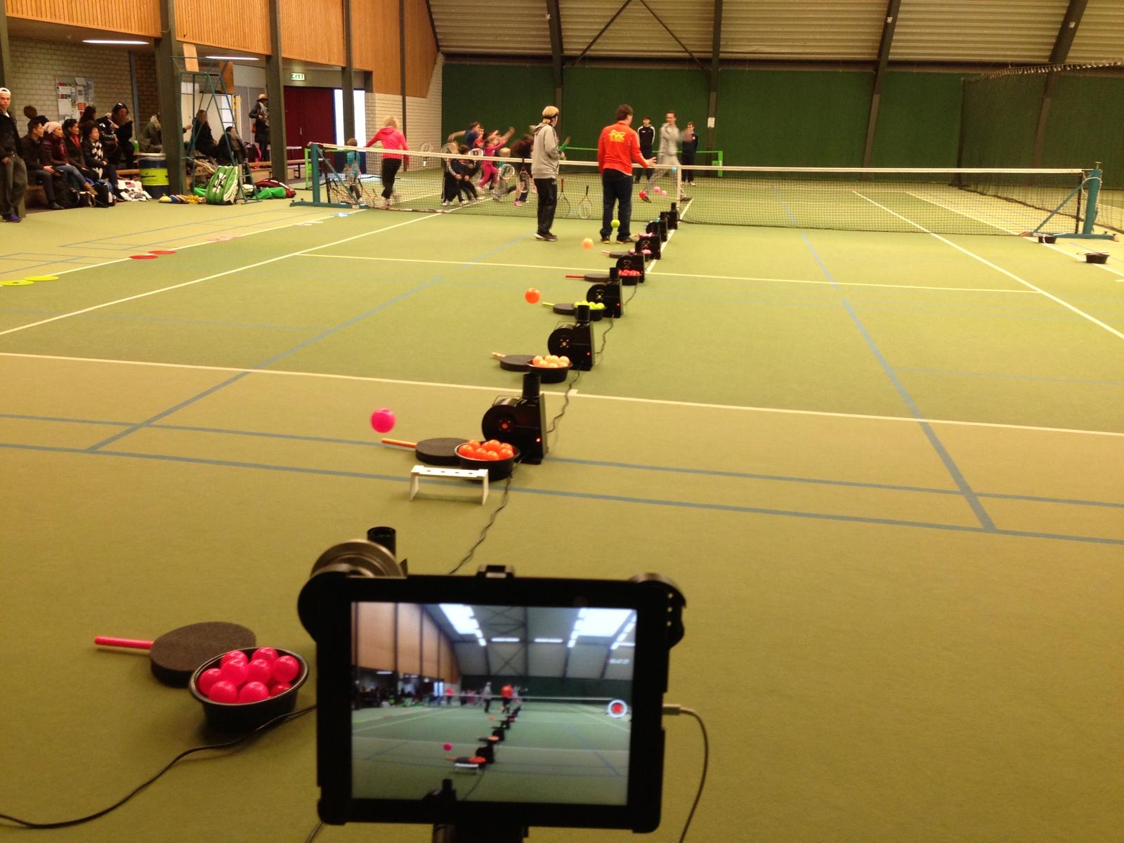 Rij floater-machines met zwevende ballen opgesteld langs het net in een tennishal